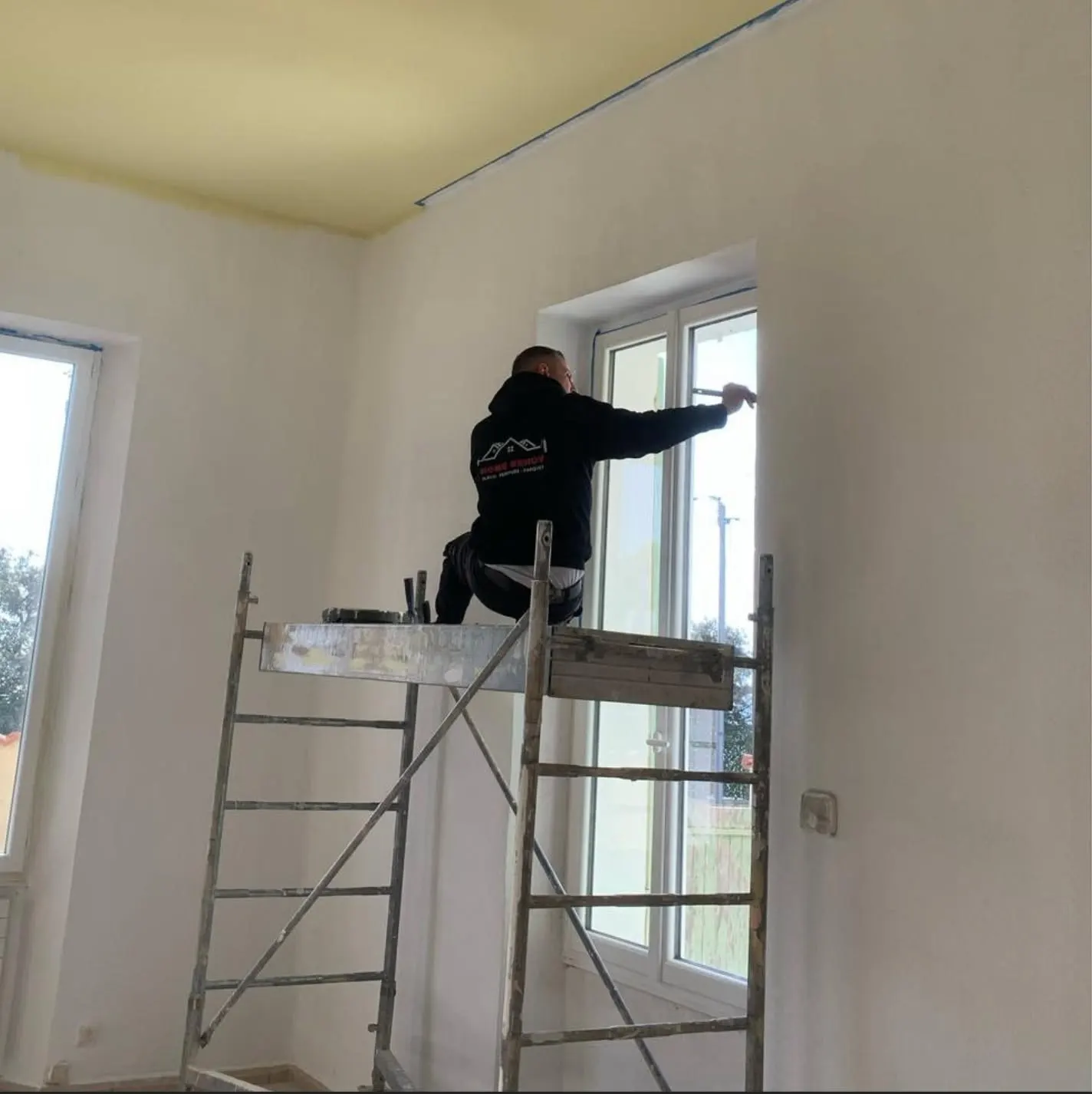 Peintre HOME RENOV sur échafaudage roulant, peinture d’une fenêtre